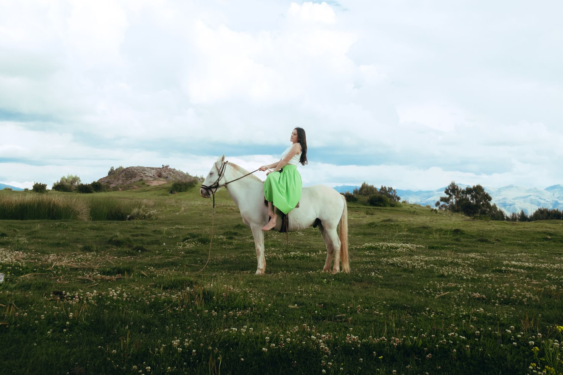 A woman rides a white horse across a lush green field